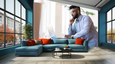 Indian young man with laptop standing in modern office background Wall mural